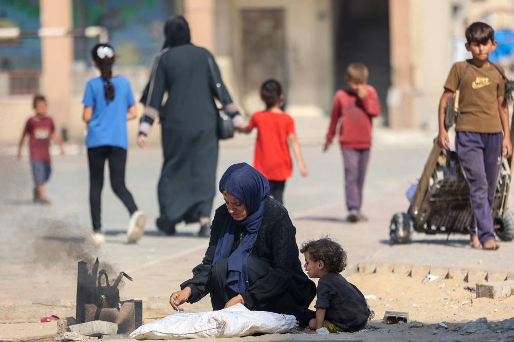 A woman cooks in a makeshift stove as Palestinians displaced by the conflict go on with their lives at the Qatari-built Hamad City residential complex in northwestern Khan Yunis, in the southern Gaza Strip, on September 24, 2025. In recent weeks, the Israeli military has launched a heavy air and ground assault on the Gaza Strip, an effort it says is aimed at eliminating Hamas fighters from the Palestinian territory's largest urban hub. (Photo by Omar AL-QATTAA / AFP)