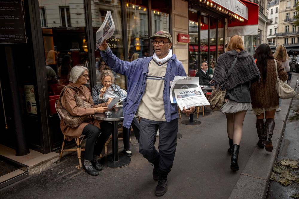 Pakistani born 73-year-old newspaper hawker Ali Akbar sells newspaper copies in the street of the Latin Quarter in Paris on September 16, 2025. Akbar, the last remaining newspaper vendor of the French capital, will be awarded by France's President as knight in the National Order of Merit. (Photo by Guillaume BAPTISTE / AFP)