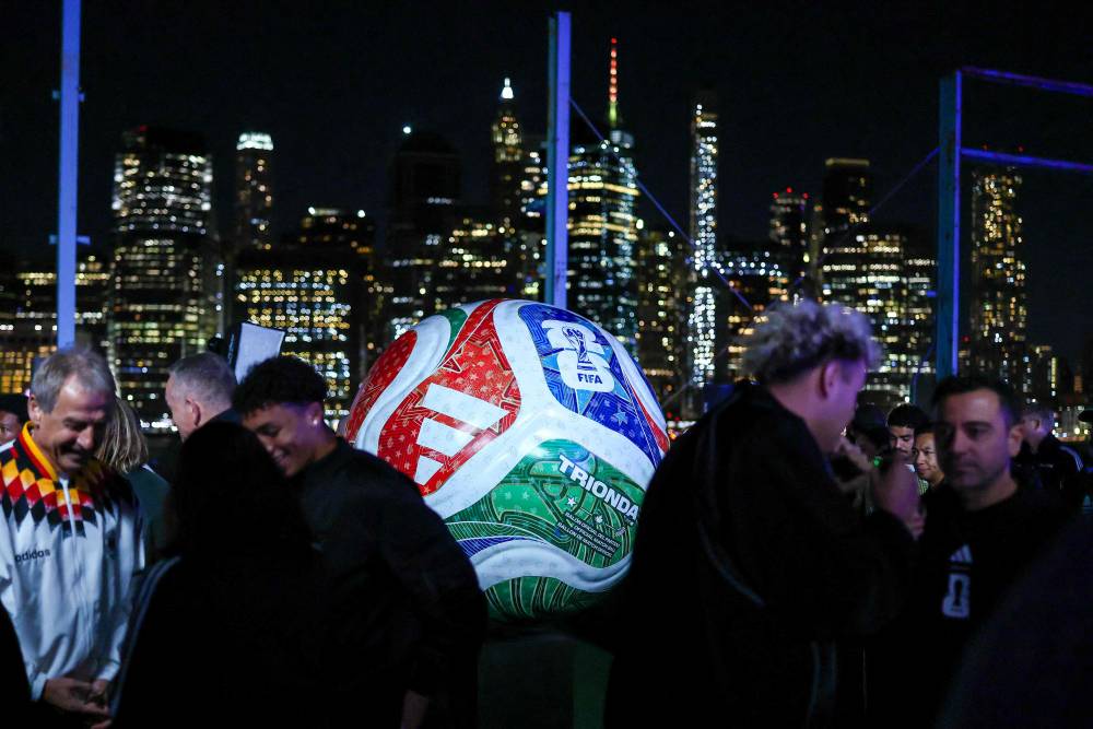 Guests chat around a large replica of the 2026 FIFA Men's World Cup match ball named Trionda during its unveiling event in New York on October 2, 2025. The 2026 FIFA Men's World Cup is scheduled to take place between June and July 2026, with matches being hosted in Mexico, Canada and the US. (Photo by CHARLY TRIBALLEAU / AFP)