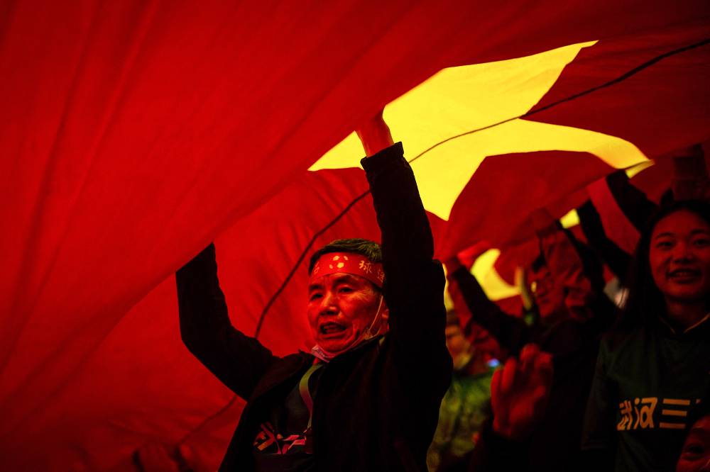 This photo taken on April 24, 2021 shows Wuhan fans passing a giant Chinese national flag as they cheer for their team during the China League One opening football match between Wuhan Three Towns FC and Beijing Institute of Technology FC in Wuhan in China's central Hubei province. (Photo by AFP)