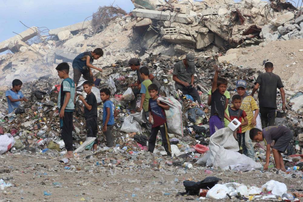 Displaced Palestinian children search of items that could be used as fuel for cooking amid a pile of garbage next to destroyed buildings at the Bureij camp for refugees in the central Gaza Strip on October 6, 2025. (Photo by Eyad BABA / AFP)