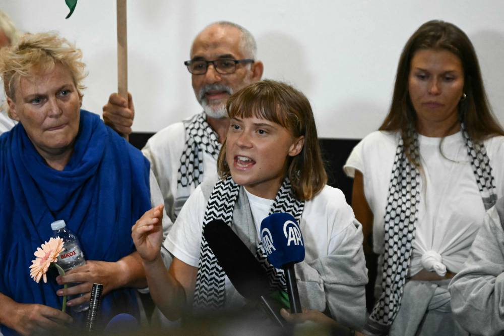 Swedish climate campaigner Greta Thunberg (C) delivers remarks upon arrival alongside activists who were sailing aboard vessels from the Gaza-bound aid flotilla before being stopped and detained by Israeli forces, greeted by a crowd of supporters, at the arrivals area of Athens International Airport on October 6, 2025. (Photo by Aris MESSINIS / AFP)