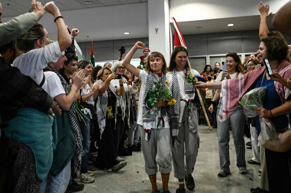 Swedish climate campaigner Greta Thunberg raises her fist, upon arrival alongside activists who were sailing aboard vessels from the Gaza-bound aid flotilla before being stopped and detained by Israeli forces, greeted by a crowd of supporters, at the arrivals area of Athens International Airport on Oct 6. Photo by Aris Messinis/AFP