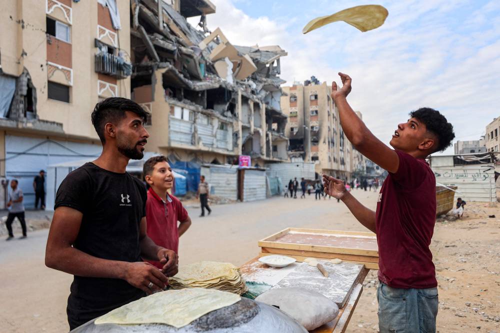 A man flips a pastry as he prepares food outside damaged buildings at the Qatari-built Hamad City residential complex in northwestern Khan Yunis, in the southern Gaza Strip, on Oct 6, 2025. Photo by Bashar Taleb/AFP