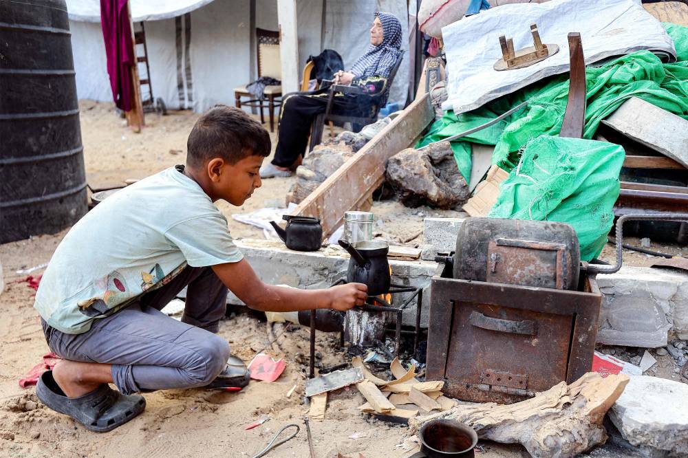 A boy monitors a pot of water boiling over a fire near tents sheltering people displaced by war at the Qatari-built and now-damaged Hamad City residential complex in northwestern Khan Yunis, in the southern Gaza Strip, on Oct 6. Photo by Omar Al-Qattaa/AFP