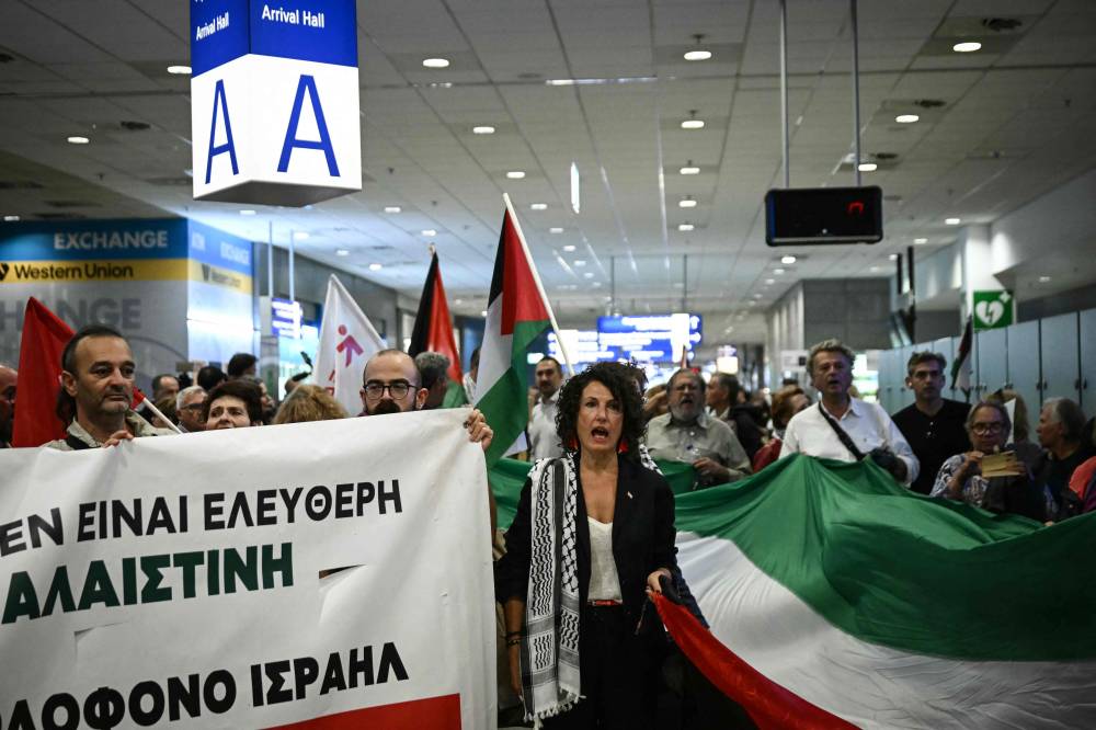 A crowd hold banners in support of the Global Sumud Flotilla at the arrivals area of Athens International Airport on October 6, 2025, as they await the return of activists who were sailing aboard vessels from the Gaza-bound aid flotilla, after Israel stopped the flotilla and detained hundreds of people. (Photo by Aris MESSINIS / AFP)
