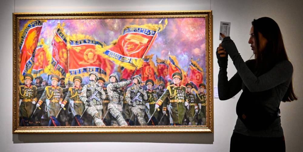 A visitor makes photos in front of the painting "Parade Column with Glorious Military Banners" by Lee Gill Ho and Jang Ba Con during North Korean arts exhibition in Moscow on October 2, 2025. (Photo by Alexander NEMENOV / AFP)