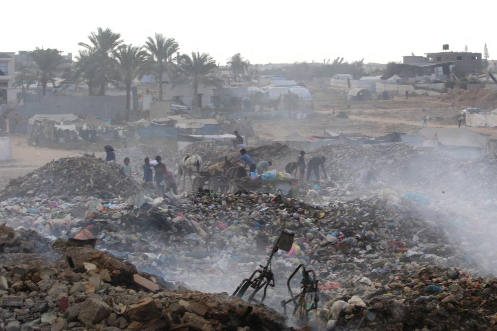 Displaced Palestinian children search of items that could be used as fuel for cooking amid a pile of burning garbage at the Bureij camp for refugees in the central Gaza Strip on Oct 6, 2025. - (Photo by EYAD BABA / AFP)
