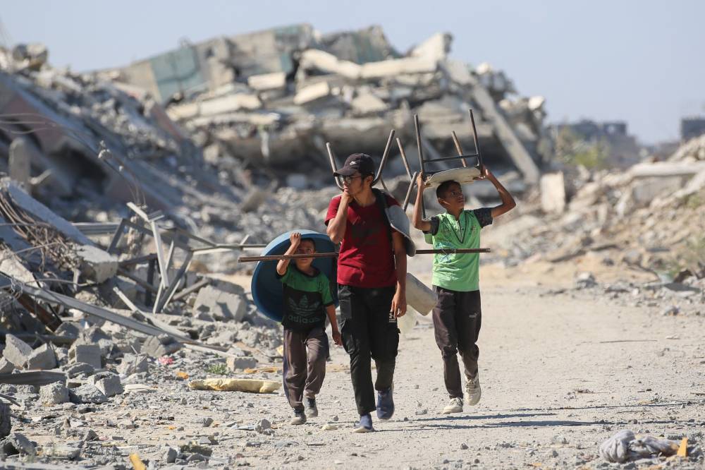 Palestinians carry chairs and a plastic basin as displaced residents return to their homes in the in al-Zahra area, north of the Nuseirat refugee camp in the central Gaza Strip, on Oct 14, 2025, a day after a ceasefire came into effect. Photo by Eyad Baba/AFP