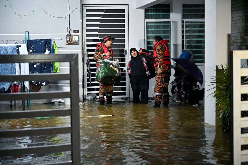 Fire and Rescue Department personnel from Kamunting assisted in relocating flood victims who were trapped inside their homes at Taman Air Putih Permai, Simpang yesterday. - Photo by Bernama