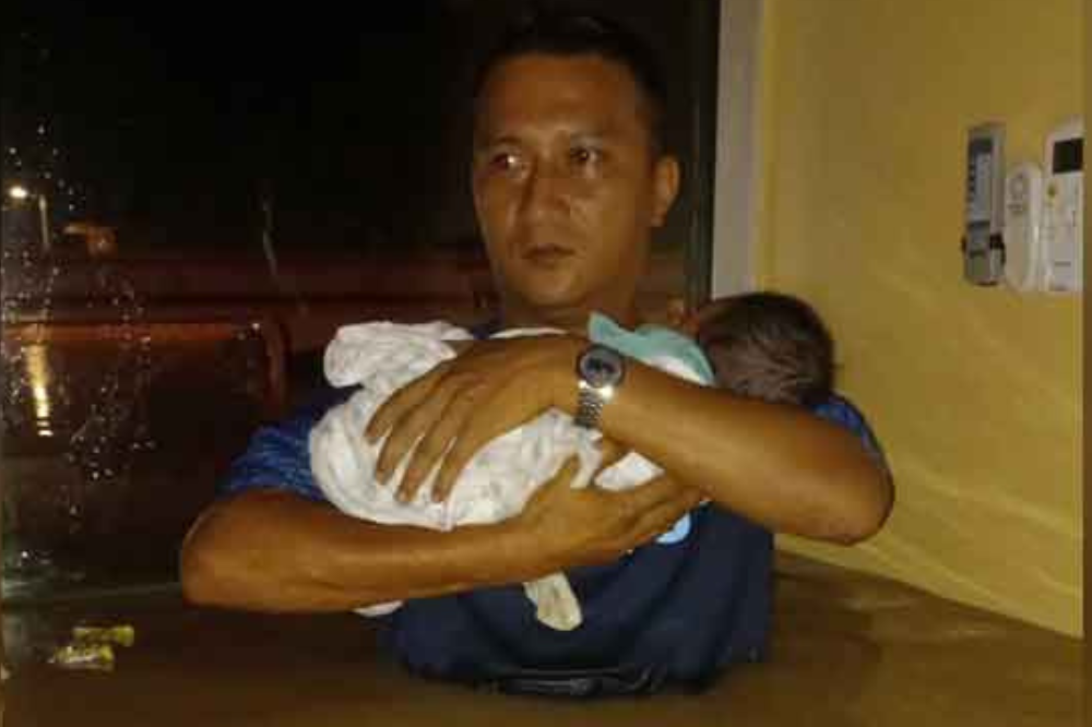 A man carrying a small baby high above the floodwaters while struggling to save himself and his family. - Photo: Social media