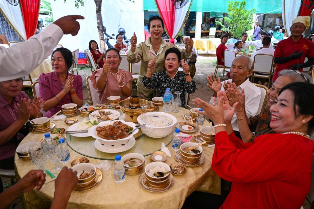 TOPSHOT - Attendees cheer as they hear the news of the signing of a ceasefire agreement between Cambodia and Thailand in Kuala Lumpur, during a wedding in Phnom Penh on October 26, 2025. (Photo by TANG CHHIN SOTHY / AFP)