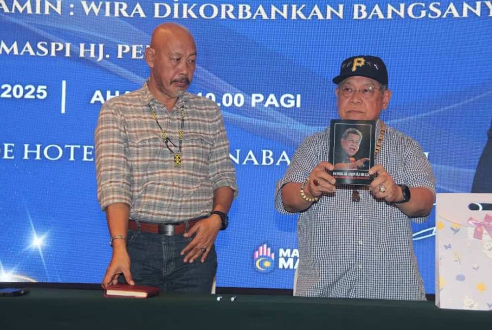 Former Dewan Rakyat Speaker Tan Sri Pandikar Amin Mulia (right) shows a book about him written by Dr Maspi Peran in Kota Kinabalu on Sunday.
