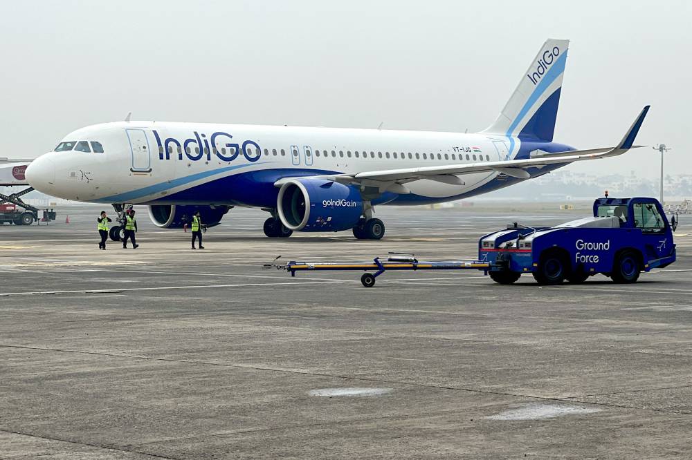 Ground staff walk past an Indigo airlines aircraft taxiing in the apron at the Netaji Subhash Chandra Bose International airport in Kolkata on February 1, 2024. India and China resume direct flights on October 26 after a five-year suspension, a move important both for trade and a symbolic step as Asia's giants cautiously rebuild relations. (Photo by Indranil MUKHERJEE / AFP)