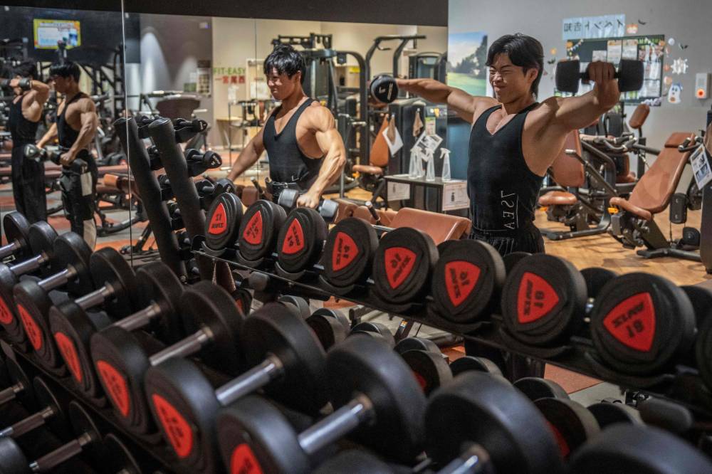 In this photograph taken on September 29, 2025, care workers and bodybuilders Takuya Usui (L) and Hokuto Tatsumi train at a gym in Ichinomiya, Aichi prefecture. Gender stereotypes and poor pay have long discouraged young men from becoming caregivers, even as demand surges in a country with one of the world's oldest populations. But Visionary, a firm based in the city of Nagoya, is successfully recruiting male bodybuilders to the care industry -- luring them to its promised "paradise for musclemen" with perks including paid gym time and protein shake subsidies. (Photo by Yuichi YAMAZAKI / AFP)