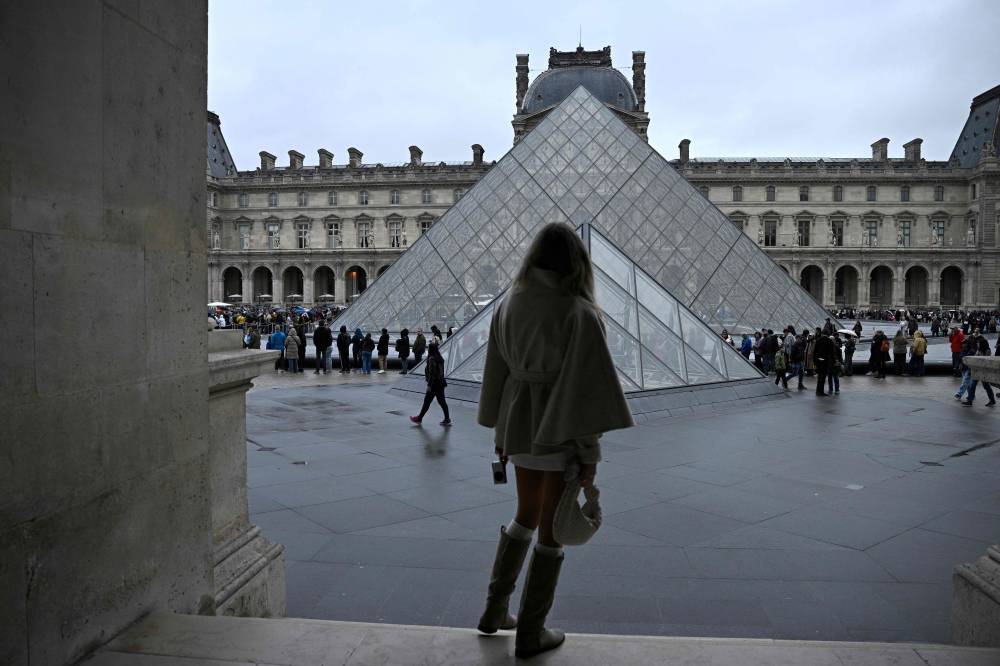 People queue in the Louvre pyramid courtyard moments before the announcement the museum will remain closed for a second day running after thieves stole crown jewels from the museum in Paris a day earlier, in Paris on Oct 20, 2025. - (Photo by JULIEN DE ROSA / AFP)