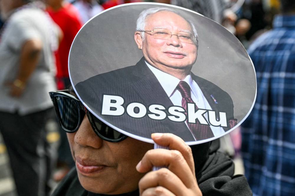 A woman holds a hand fan bearing a photo of former prime minister Datuk Seri Najib Razak and reading "Bossku" as supporters gather for his appeal hearing outside the Palace of Justice in Putrajaya on Jan 6, 2025. - (Photo by MOHD RASFAN / AFP)