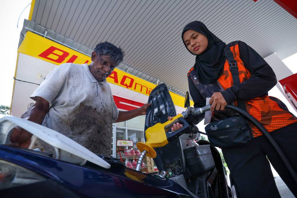 Rubber tapper Rajindran Muniandi, 67, being assisted by petrol station attendant Anis Nabika Ismady, 22, while refueling under the Budi Madani RON95 (Budi95) initiative at a subsidiSed price of RM1.99 per litre compared to the market price of RM2.60 per litre, at Kampung Felda Hutan Percha, recently. - Bernama photo