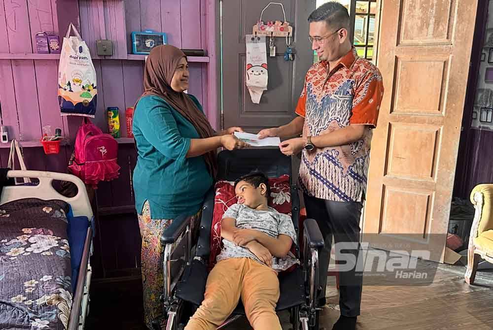 Nik Nur Atiqah (left) receives a cash donation and a wheelchair from ISejahtera, presented by its chairman, Mohammad Hamizan (right). — Photo by Adila Sharinni Wahid / Sinar 
