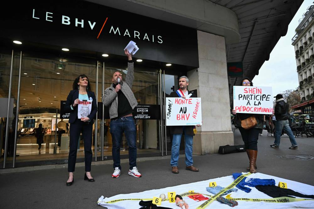 Arnaud Gallais (C), president of Mouv'Enfants, a movement fighting against all forms of violence against children, next to Ecologiste et Social's MP Arnaud Bonnet (2nd-R) holding a placard reading "shame to BHV", takes part with activists in a protest in front of the BHV department store in Paris on Nov 3, 2025, after Chinese company Shein was selling dolls of a likely "child pornography nature". - (Photo by JULIE SEBADELHA / AFP)
