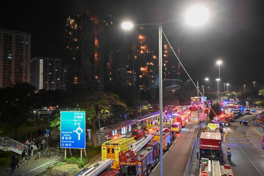 Fire trucks and rescue vehicles line a road during a major fire at the Wang Fuk Court residential estate (background) in Hong Kong's Tai Po district. Photo by Peter Parks/AFP