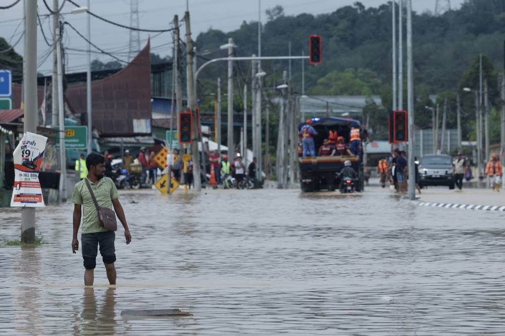 Village residents wade through floodwaters that have submerged the main road in Kampung Sungai Serai. Photo by Bernama