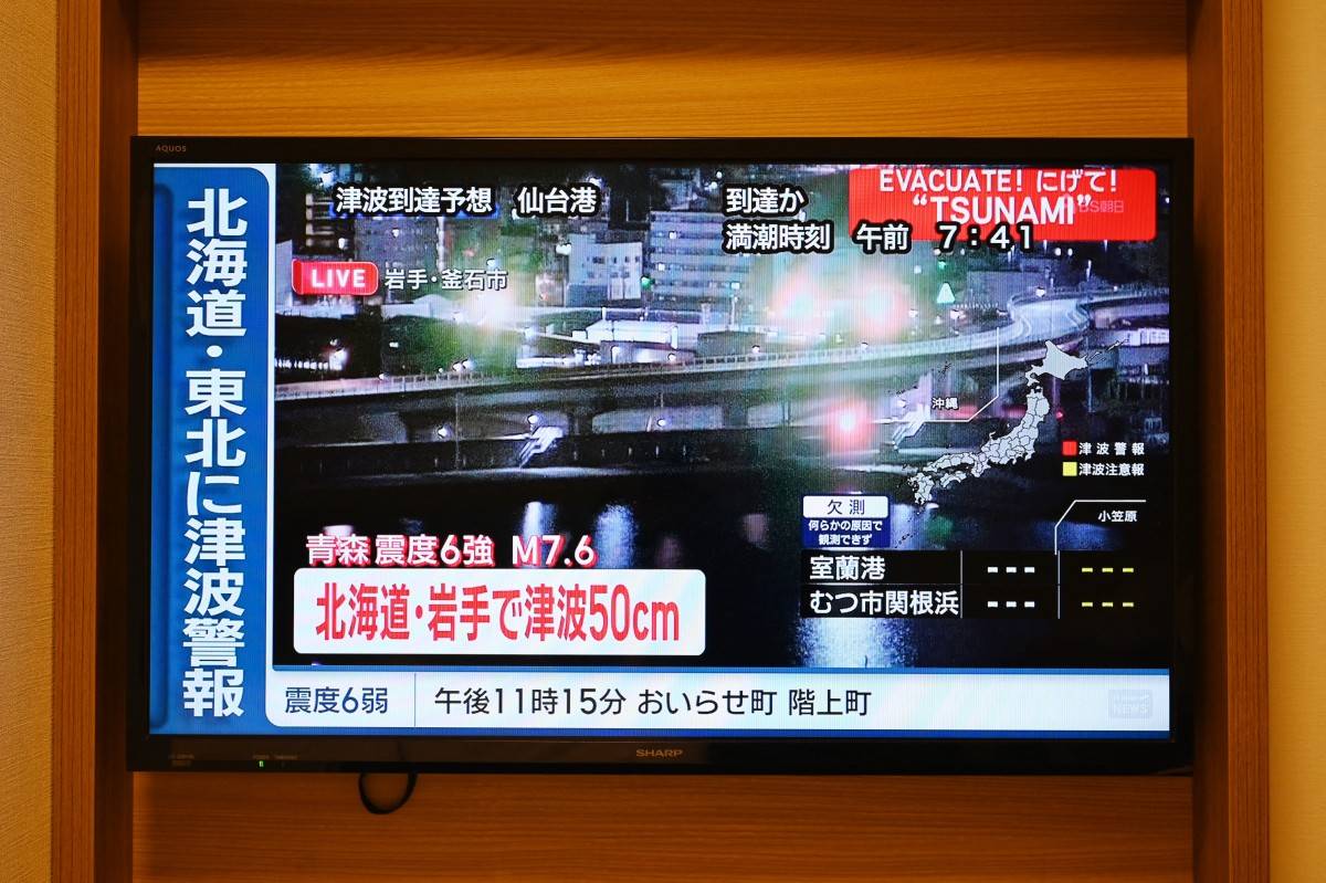 A tsunami warning flashes over live footage of a waterfront area, on a television screen in Sapporo, in Japan’s northern Hokkaido prefecture on Dec 9, 2025. - (Photo by GREG BAKER / AFP)