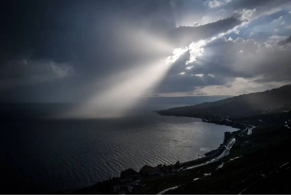 A ray of sun shines through clouds over Lake Geneva next to the Lavaux vineyard terraces near Chexbres, western Switzerland, on August 8, 2018. (Photo by Fabrice COFFRINI / AFP)