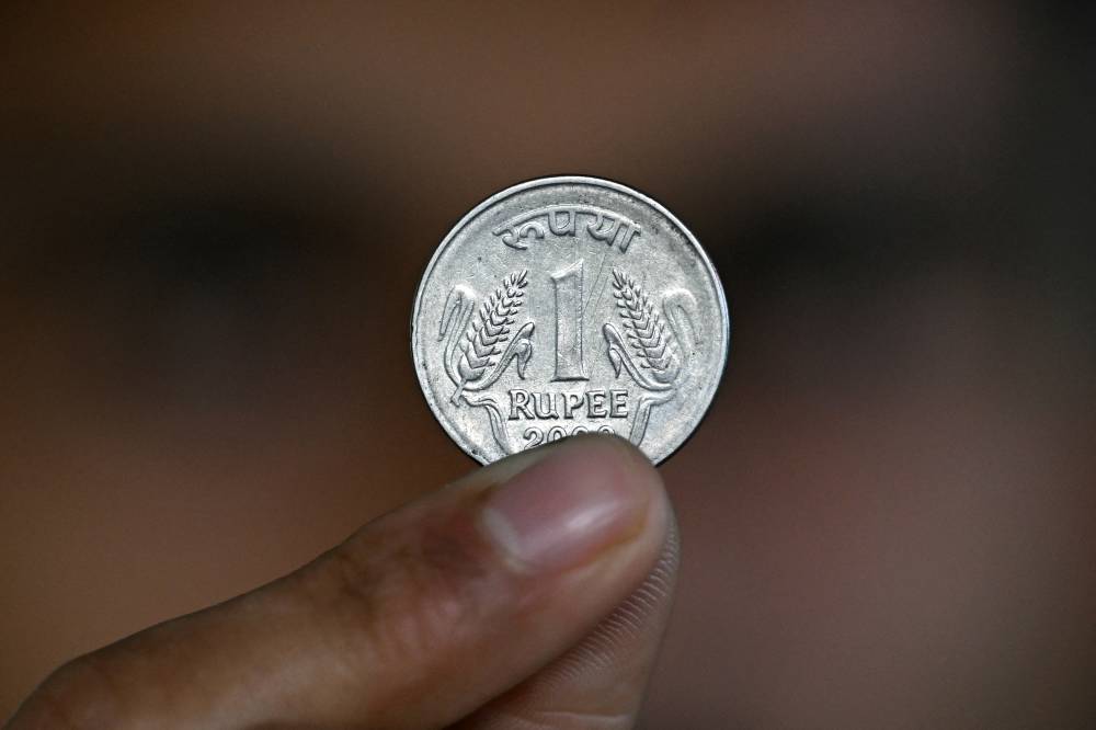 This photo illustration shows an employee holding an Indian rupee coin at an office in Bengaluru on December 5, 2025. (Photo by Idrees MOHAMMED / AFP)