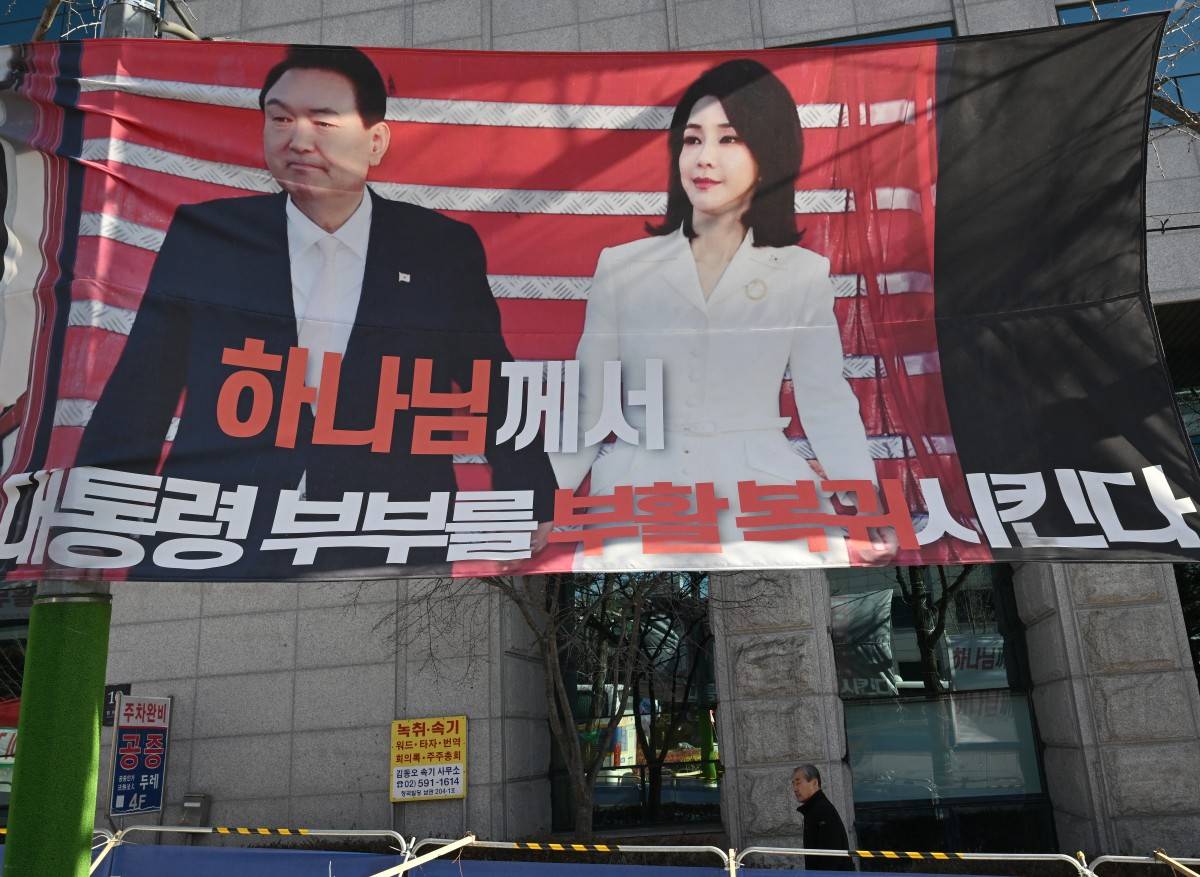 A man walks past a banner showing a picture of South Korea's former impeached president Yoon Suk Yeol and his wife Kim Keon Hee, on a street near the Seoul Central District Court in Seoul. Photo by Jung Yeon-je/AFP