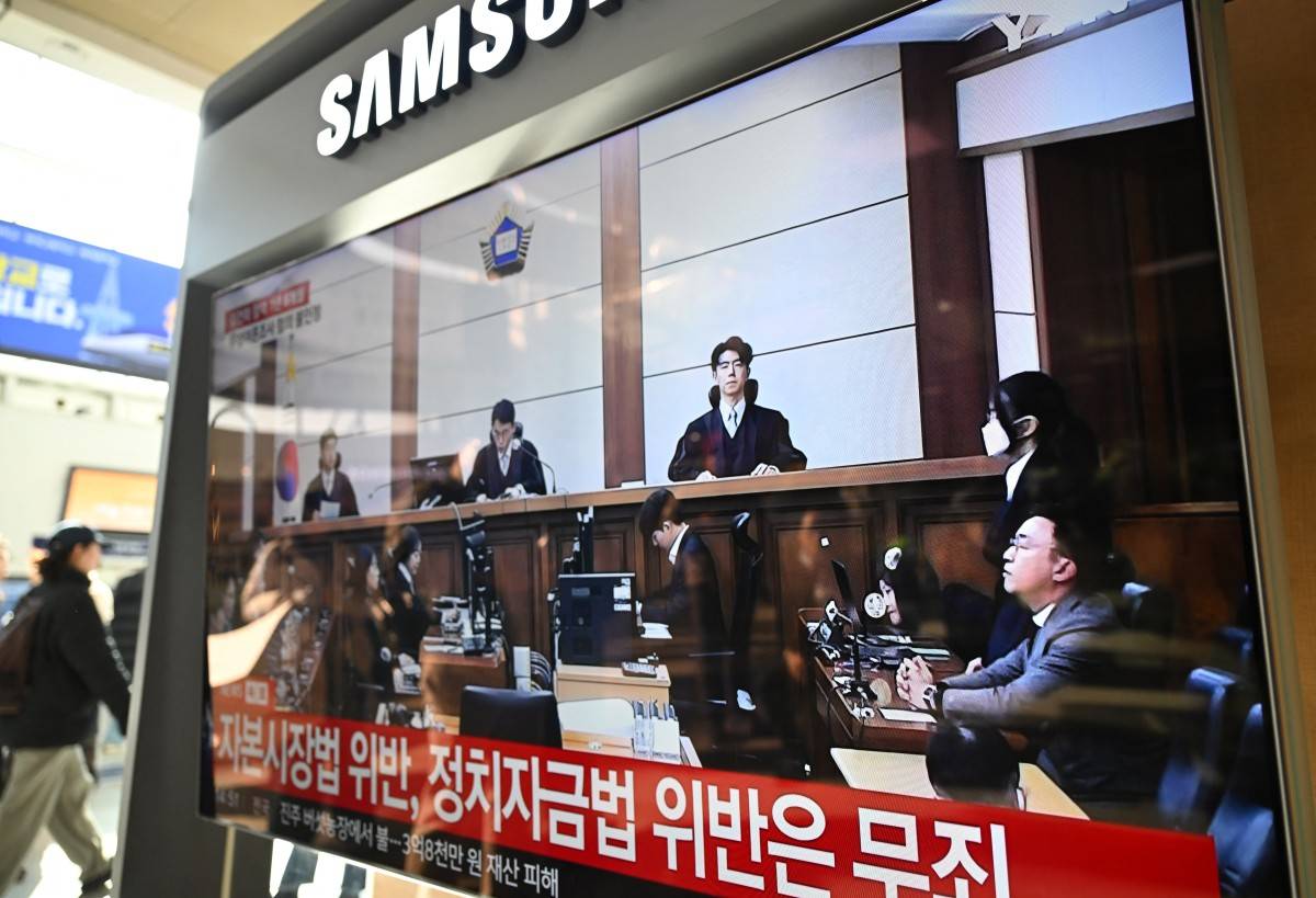 A man walks past a television screen showing a live broadcast of the trial verdict on corruption charges of South Korea's former first lady Kim Keon Hee (R with a mask on the screen), at a train station in Seoul. Photo by Jung Yeon-je/AFP