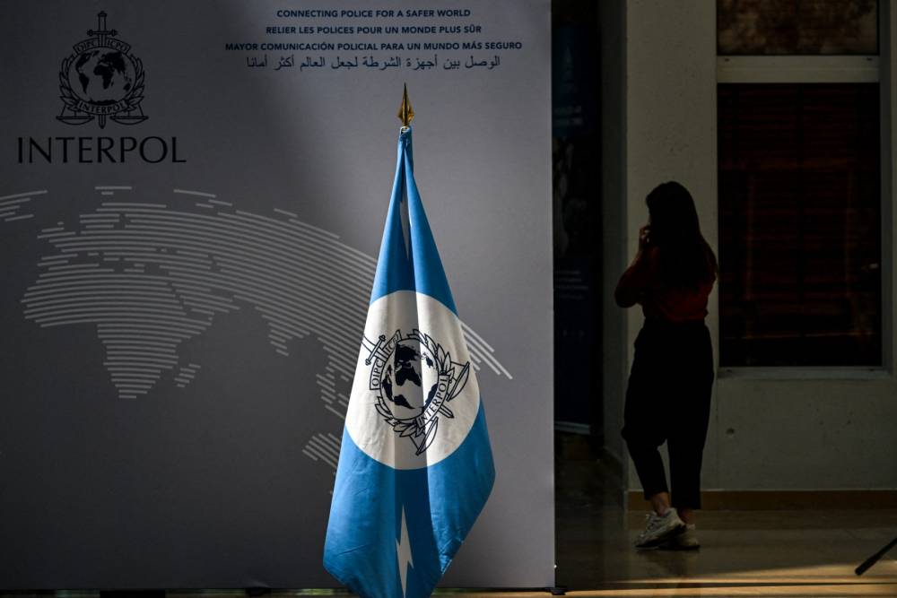 A woman walks near an Interpol flag ahead at the International Criminal Police Organisation Interpol headquarters in Lyon, eastern France, on June 9, 2025. (Photo by OLIVIER CHASSIGNOLE / AFP)
