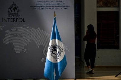 A woman walks near an Interpol flag ahead at the International Criminal Police Organisation Interpol headquarters in Lyon, eastern France, on June 9, 2025. (Photo by OLIVIER CHASSIGNOLE / AFP)