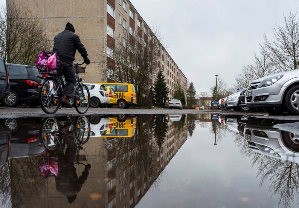An elderly man is reflected in a puddle as he cycles through a residential area consisting of "Plattenbau" prefabricated buildings dating back to Communist east German times in Fuerstenwalde, eastern Germany, on January 19, 2018. (Photo by John MACDOUGALL / AFP)