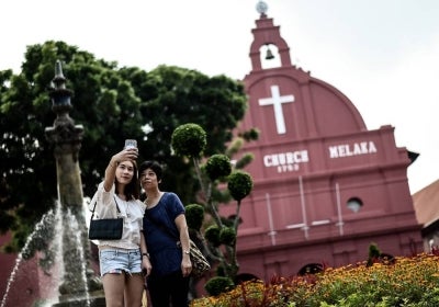 Tourists pose for a selfie in front of the 18th-century Anglican church in Malaysia's historical city of Malacca. (Photo by MANAN VATSYAYANA / AFP) AFP file photo for illustration purpose only