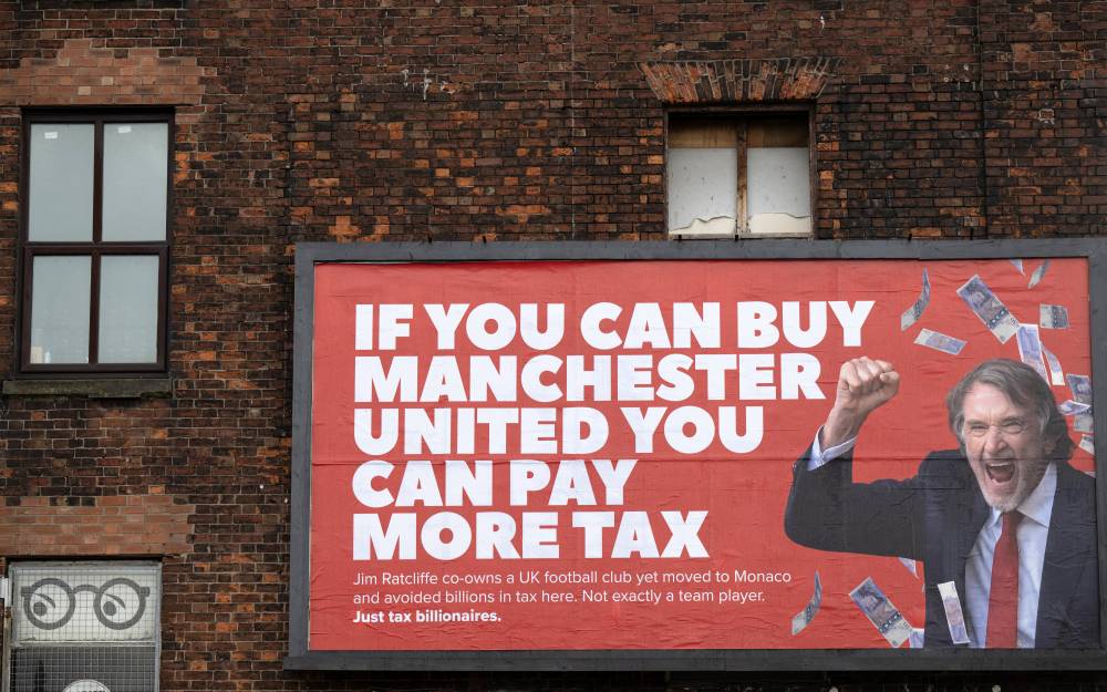 A billboard poster created by the campaign group 'Everyone Hates Elon', and featuring an image of Manchester United co-owner, and CEO of INEOS chemicals group, Jim Ratcliffe, with the slogan "If you can buy Manchester United you can pay more tax", is pictured in Manchester, north west England on November 11, 2025. (Photo by Oli SCARFF / AFP)