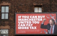 A billboard poster created by the campaign group 'Everyone Hates Elon', and featuring an image of Manchester United co-owner, and CEO of INEOS chemicals group, Jim Ratcliffe, with the slogan "If you can buy Manchester United you can pay more tax", is pictured in Manchester, north west England on November 11, 2025. (Photo by Oli SCARFF / AFP)