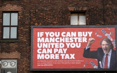 A billboard poster created by the campaign group 'Everyone Hates Elon', and featuring an image of Manchester United co-owner, and CEO of INEOS chemicals group, Jim Ratcliffe, with the slogan "If you can buy Manchester United you can pay more tax", is pictured in Manchester, north west England on November 11, 2025. (Photo by Oli SCARFF / AFP)