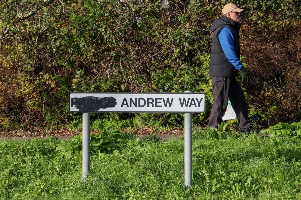 A pedestrian walks past a sign for a street originally named after Britain's former prince Andrew, with the title of "prince" blackened out, along a road in the town of Carrickfergus, County Antrim in Northern Ireland on November 25, 2025. A Northern Irish council has voted to rename a street in the town of Carrickfergus called after Britain's disgraced former prince Andrew. Mid and East Antrim is the first UK council to drop the ex-prince from a street name following King Charles III's decision to remove his brother -- now known as Andrew Mountbatten Windsor -- from public life. (Photo by Paul Faith / AFP)