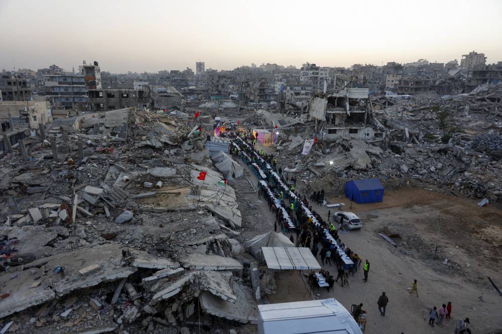 Palestinians gather for a mass fast-breaking iftar meal organised by the Turkish IHH Foundation, amid the rubble of destroyed buildings in Gaza City on Feb 18, 2026. - (Photo by OMAR AL-QATTAA / AFP)