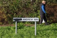 A pedestrian walks past a sign for a street originally named after Britain's former prince Andrew, with the title of "prince" blackened out, along a road in the town of Carrickfergus, County Antrim in Northern Ireland on November 25, 2025. A Northern Irish council has voted to rename a street in the town of Carrickfergus called after Britain's disgraced former prince Andrew. Mid and East Antrim is the first UK council to drop the ex-prince from a street name following King Charles III's decision to remove his brother -- now known as Andrew Mountbatten Windsor -- from public life. (Photo by Paul Faith / AFP)