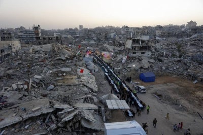 Palestinians gather for a mass fast-breaking iftar meal organised by the Turkish IHH Foundation, amid the rubble of destroyed buildings in Gaza City on Feb 18, 2026. - (Photo by OMAR AL-QATTAA / AFP)