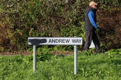 A pedestrian walks past a sign for a street originally named after Britain's former prince Andrew, with the title of "prince" blackened out, along a road in the town of Carrickfergus, County Antrim in Northern Ireland on November 25, 2025. A Northern Irish council has voted to rename a street in the town of Carrickfergus called after Britain's disgraced former prince Andrew. Mid and East Antrim is the first UK council to drop the ex-prince from a street name following King Charles III's decision to remove his brother -- now known as Andrew Mountbatten Windsor -- from public life. (Photo by Paul Faith / AFP)