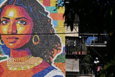 Venezuelan artist Oscar Olivares (R) poses next to his mural made with plastic bottle caps on an apartment building in the Zacamil neighborhood in Mejicanos, El Salvador, on February 20, 2026. The artwork, over 13 meters tall and made with more than 100,000 recycled plastic bottle caps, is regarded as the world's tallest bottle-cap mural. The piece reinterprets the Mona Lisa with a Latin American identity and pays tribute to Salvadoran women. (Photo by Marvin RECINOS / AFP)