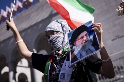 A protester holds a portrait of Iran's supreme leader Ayatollah Ali Khamenei and a flag of Iran during a demonstration against the war in Iran in front of City Hall in Los Angeles, California, on February 28, 2026. (Photo by ETIENNE LAURENT / AFP)