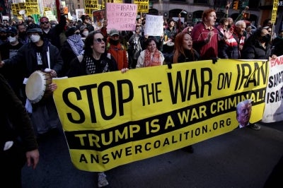 People hold signs and a banner during the "Stop the War on Iran" protest at Times Square in New York City on February 28, 2026. (Photo by Leonardo MUNOZ / AFP)