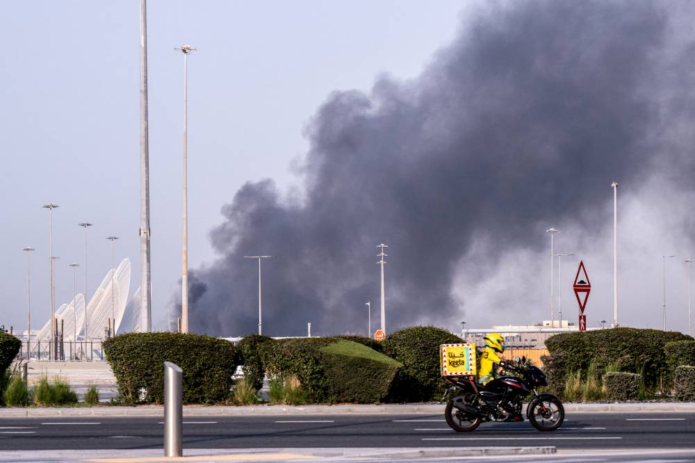 A food delivery bike drive close to a plume of smoke rising from the Zayed Port following a reported Iranian strike in Abu Dhabi on March 1, 2026. Iran's retaliatory missile and drone campaign in the Gulf has killed three people and wounded 58 in the United Arab Emirates since it began, Emirati authorities said on March 1, the day after the US and Israel launched a nationwaide attack on Iran killing its supreme leader. (Photo by Ryan Lim / AFP)