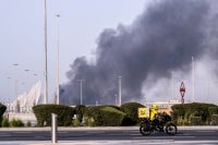 A food delivery bike drive close to a plume of smoke rising from the Zayed Port following a reported Iranian strike in Abu Dhabi on March 1, 2026. Iran's retaliatory missile and drone campaign in the Gulf has killed three people and wounded 58 in the United Arab Emirates since it began, Emirati authorities said on March 1, the day after the US and Israel launched a nationwaide attack on Iran killing its supreme leader. (Photo by Ryan Lim / AFP)