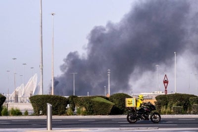 A food delivery bike drive close to a plume of smoke rising from the Zayed Port following a reported Iranian strike in Abu Dhabi on March 1, 2026. - (Photo by Ryan Lim / AFP)