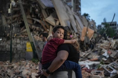 People walk past a collapsed building following an earthquake in Caracas on June 25, 2026. Powerful twin earthquakes have killed 32 people and injured more than 700, the nation's interim president said on June 25, after the massive shocks collapsed entire buildings and sent people running in panic. (Photo by AFP)